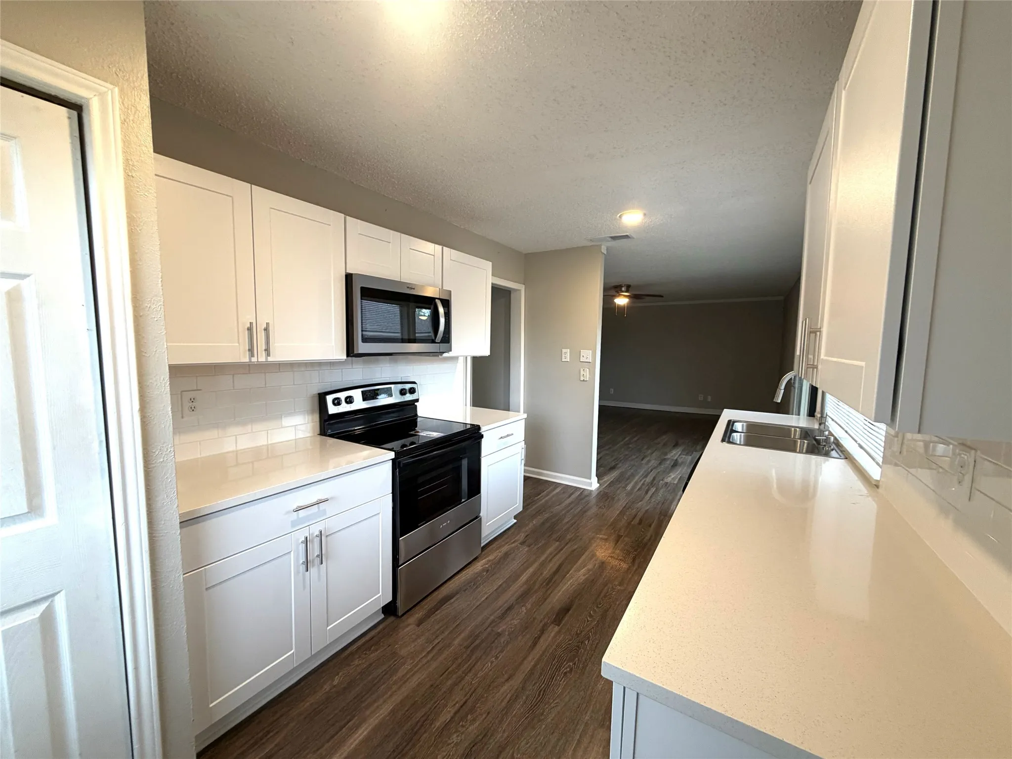 Kitchen featuring white shaker cabinetry, stainless steel appliances, white subway tile backsplash, light-toned countertops, and wood-finish flooring