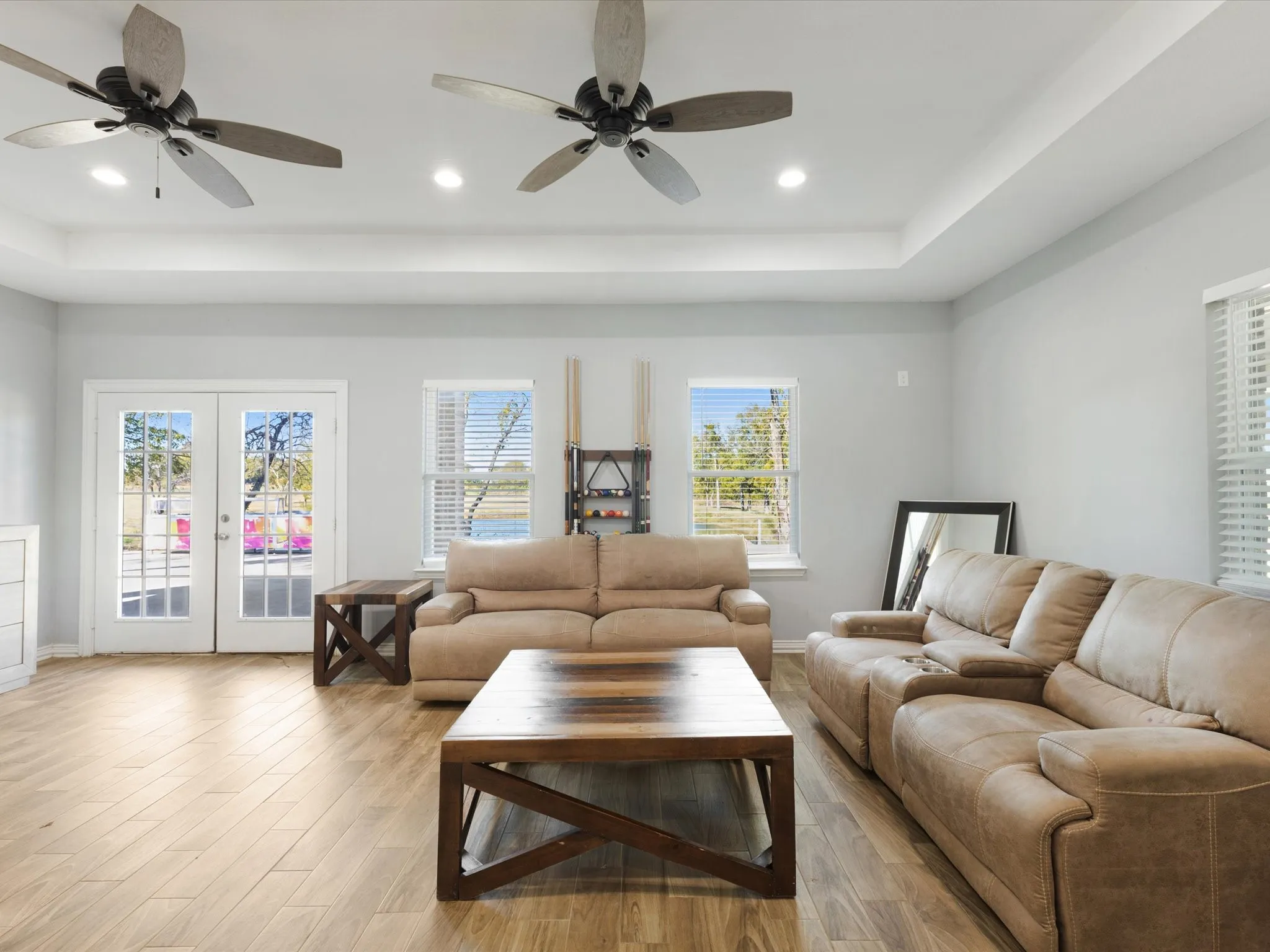 Wood-finish tile flooring throughout, white double French doors, large windows with blinds, recessed lighting, and a tray ceiling