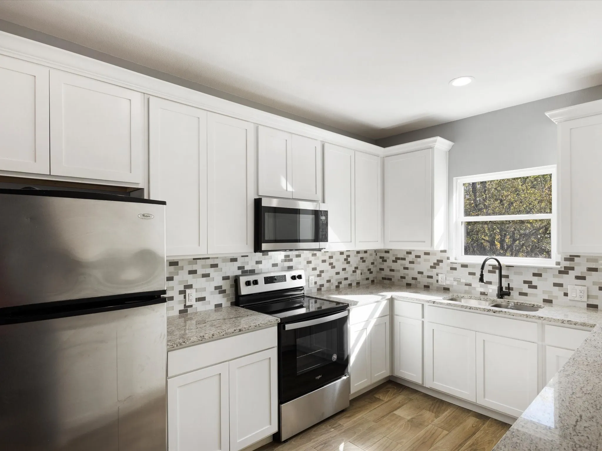 White shaker-style cabinetry, granite countertops, mosaic tile backsplash, stainless steel appliances, and wood-finish flooring