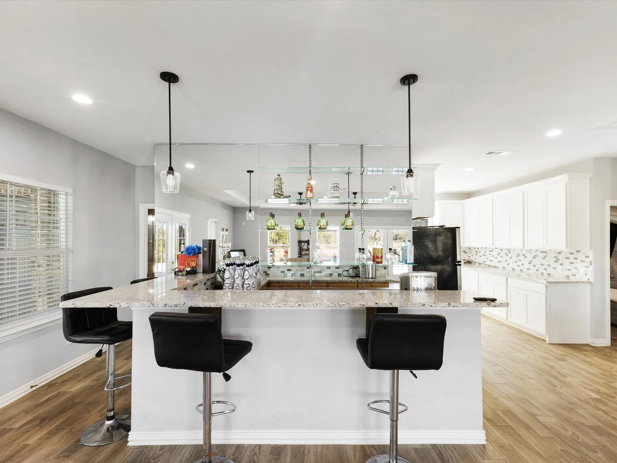 Extended kitchen island with a light-toned countertop, wood-finish flooring, white cabinetry, and a mosaic tile backsplash