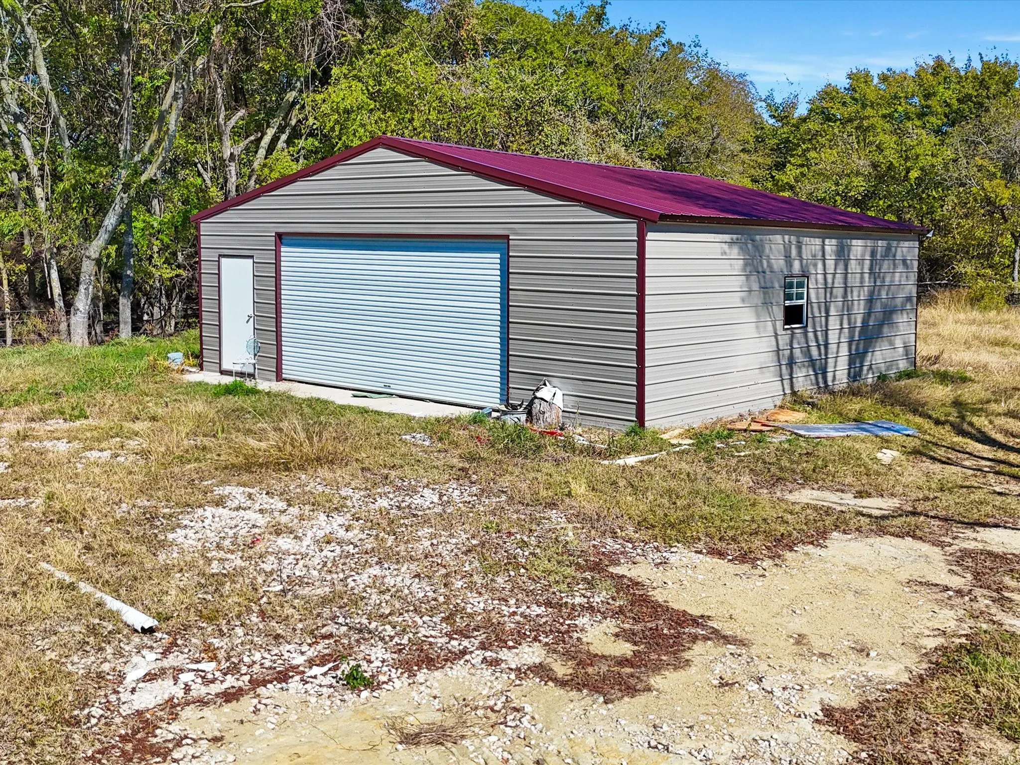 Metal utility building with a maroon-colored roof and light blue roll-up door