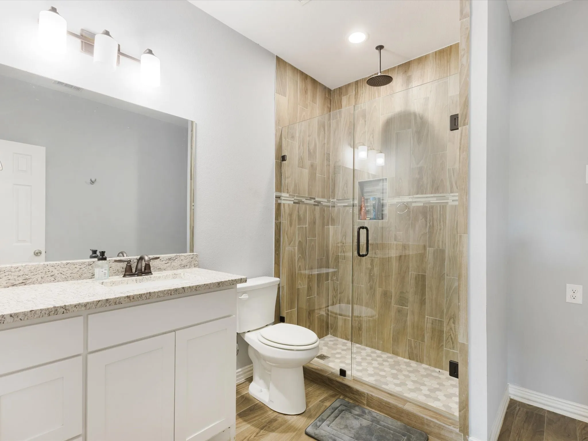Glass-enclosed shower with a rainfall showerhead, wood-finish tile surround, and hexagonal floor tiles