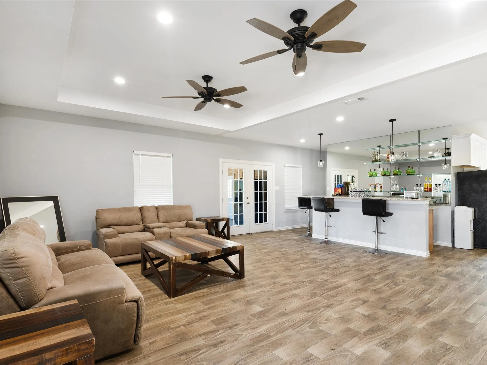 Tray ceiling with recessed lighting, two ceiling fans, French doors, wood-finish flooring, built-in bar with shelving and pendant lighting