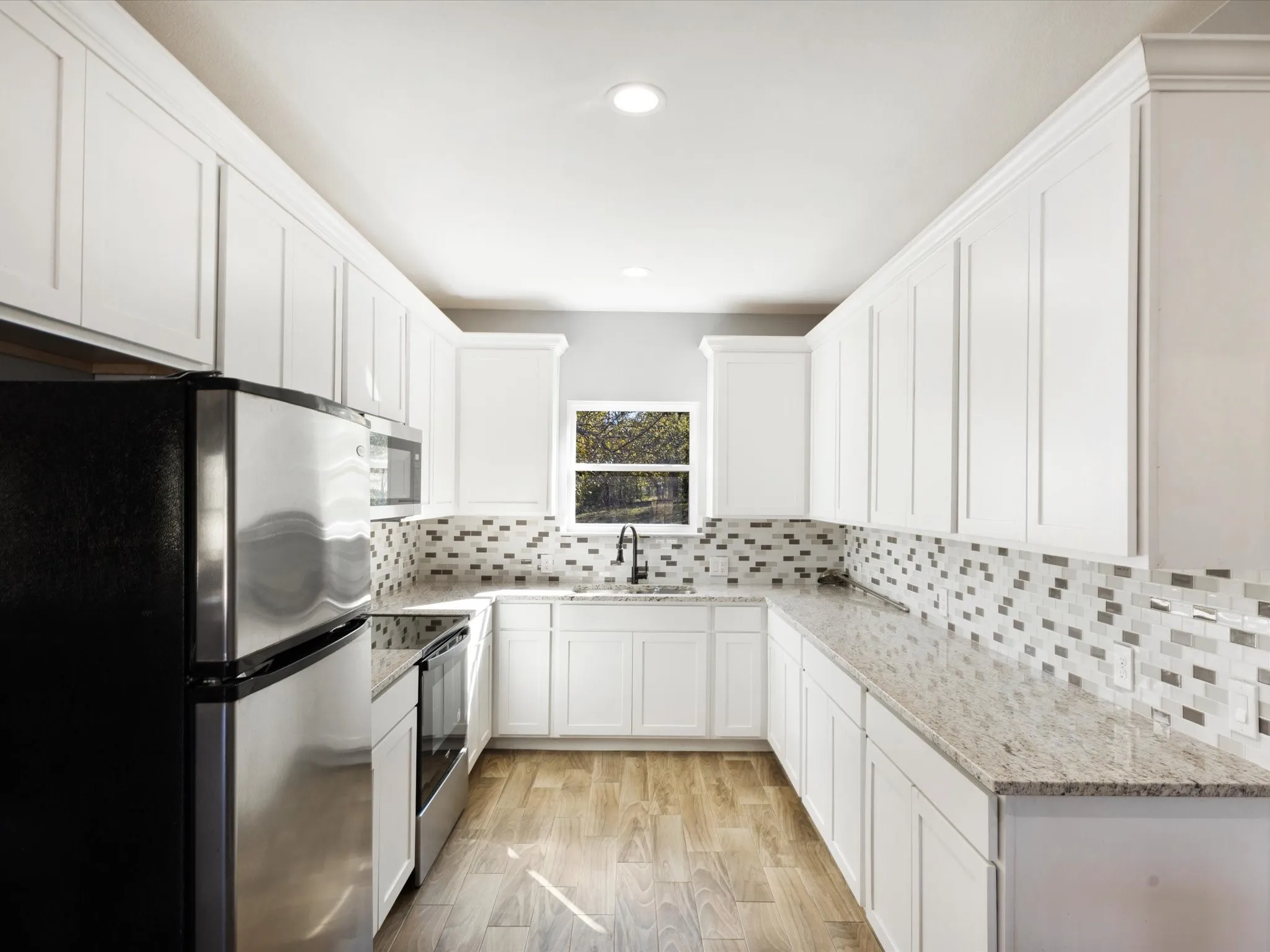 U-shaped kitchen featuring white cabinetry, granite countertops, a mosaic tile backsplash, stainless steel appliances, and wood-finish flooring