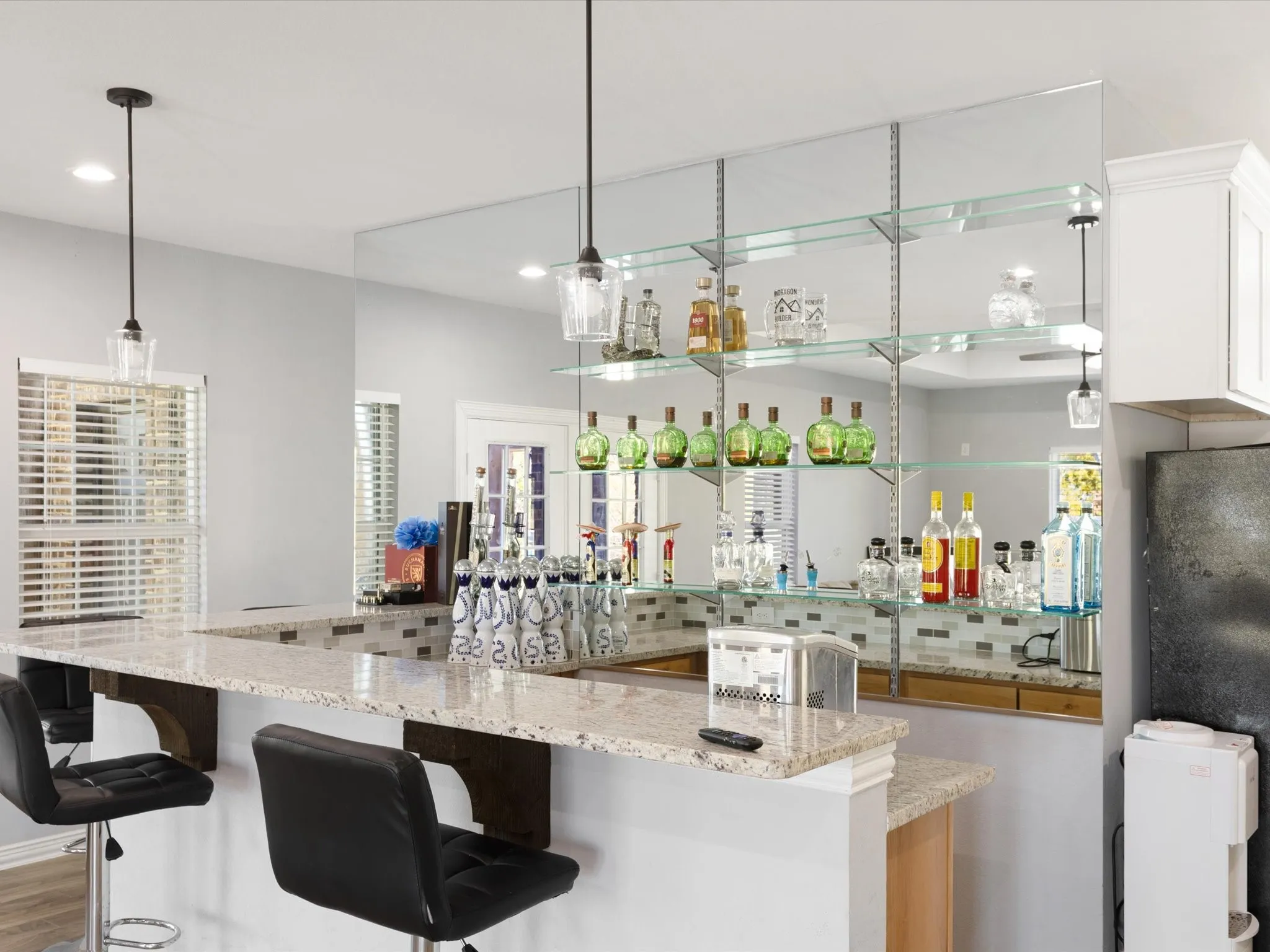Built-in bar featuring a stone countertop, mirrored wall, glass shelving, and pendant lighting