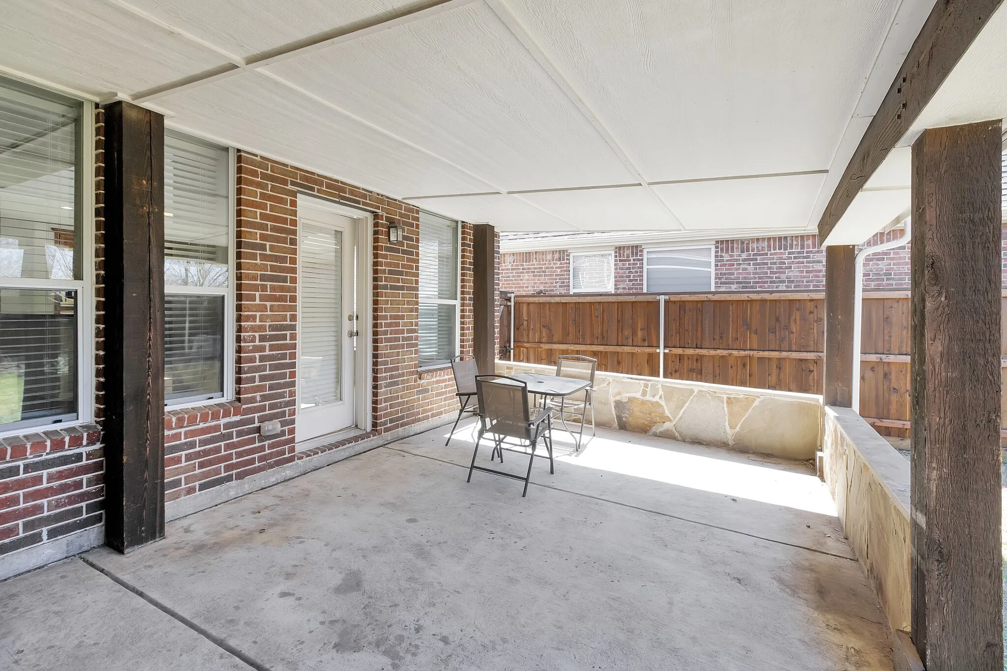 Covered patio featuring concrete flooring, wood support columns, and a brick exterior wall