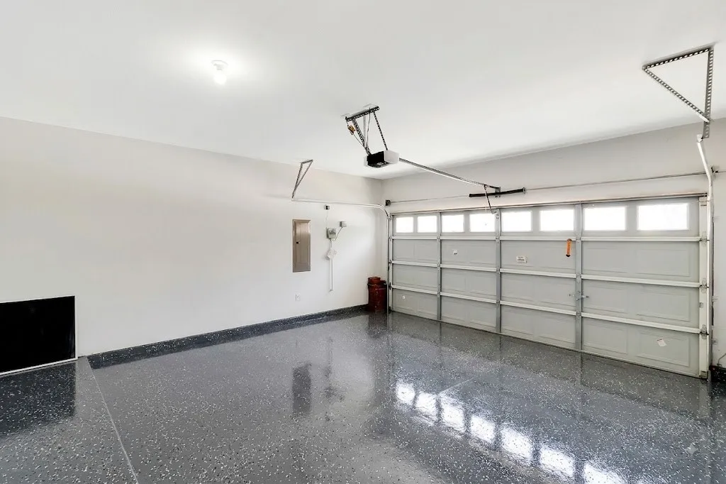 Spacious garage featuring a durable epoxy floor, an automatic overhead door with integrated windows, and a ceiling-mounted light fixture