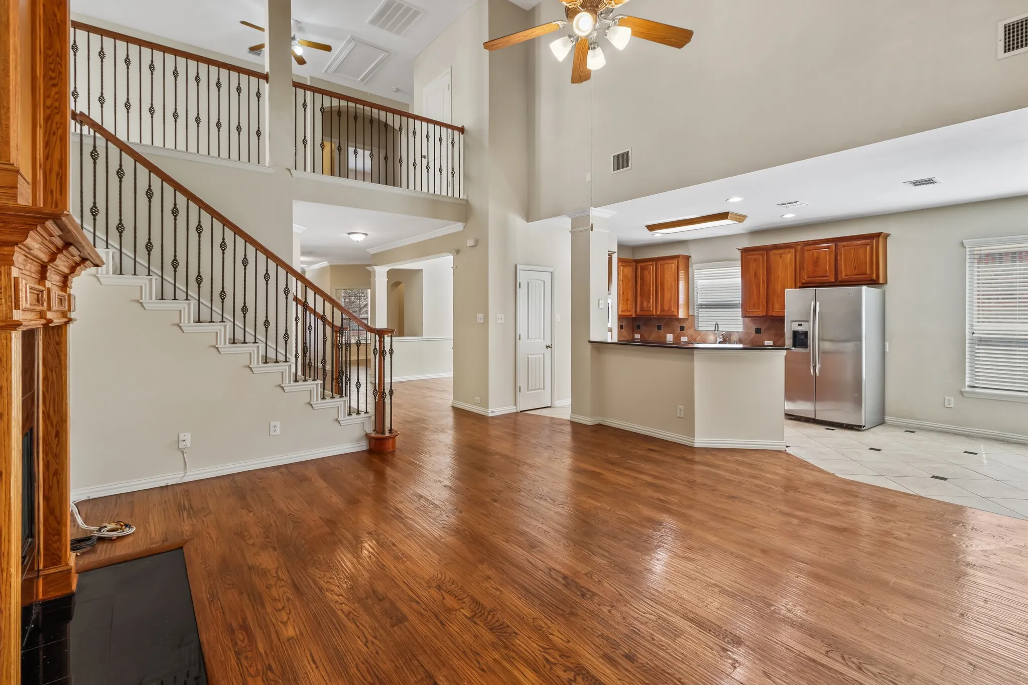 Two-story living area featuring wood-finish flooring, a grand staircase with wrought iron balusters, a kitchen with wood cabinetry, and a ceiling fan