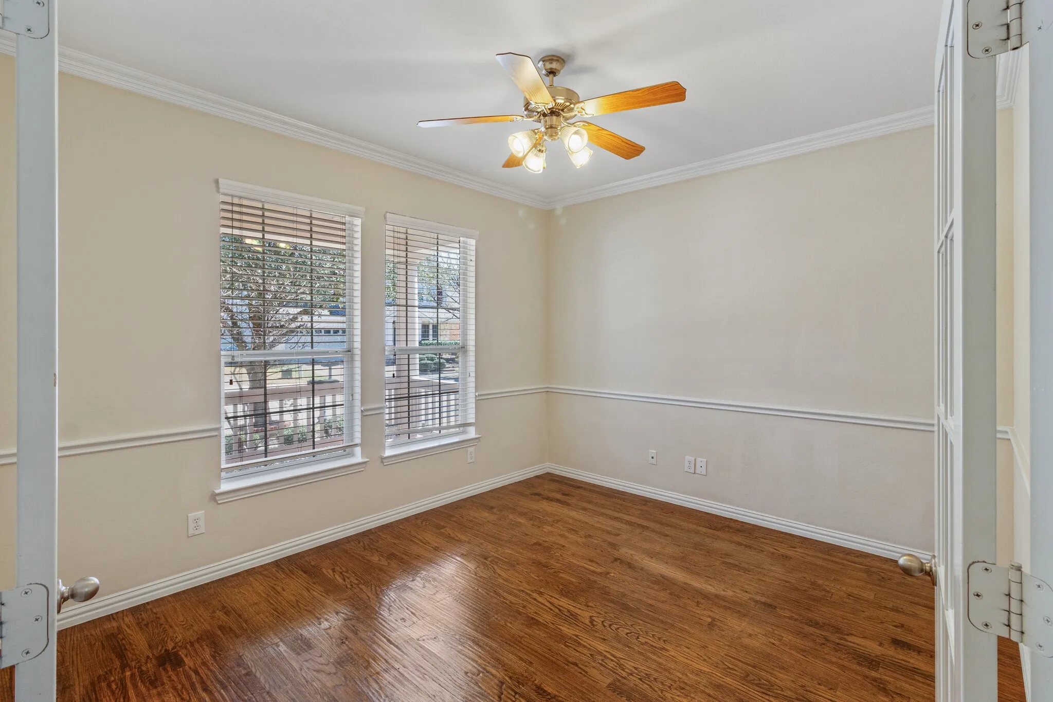 Hardwood flooring, dual windows with blinds, crown molding, chair rail molding, and a ceiling fan with light fixture
