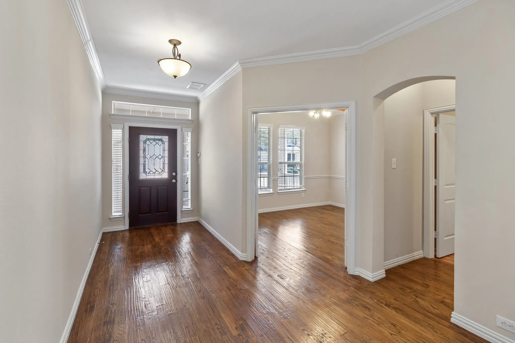 Wood-finish flooring throughout, crown molding detailing, and an arched entry
