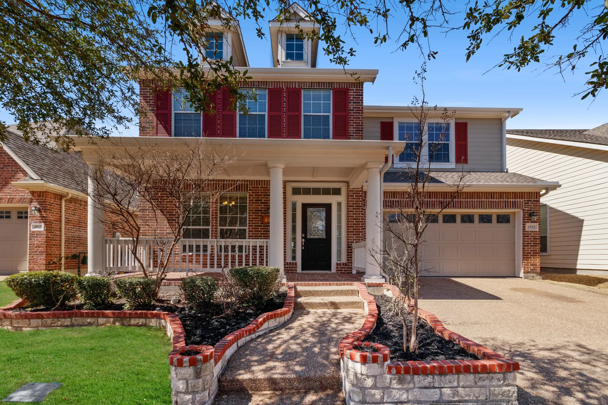 Brick facade with shutters, covered front porch, integrated two-car garage, and a decorative brick and stone planter