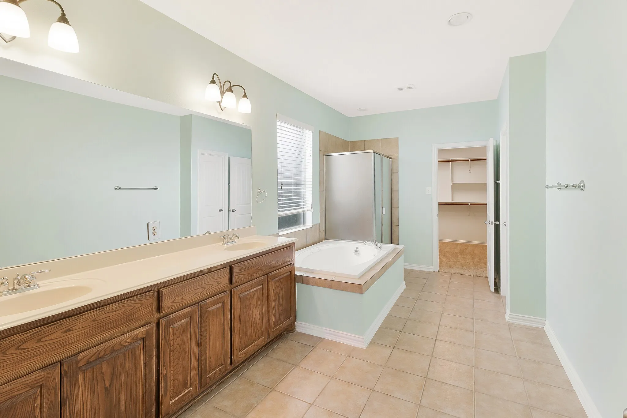 Dual wood-finish vanity with integrated sinks, built-in soaking tub, tiled shower enclosure, and tiled flooring