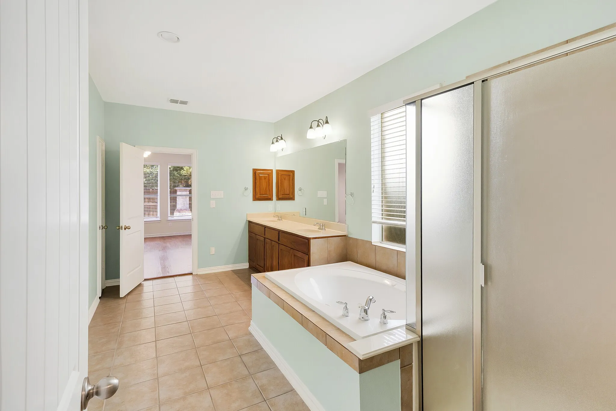 Tiled flooring, dual vanity with wood-finish cabinetry and light-toned countertops, built-in bathtub, and a glass-enclosed shower