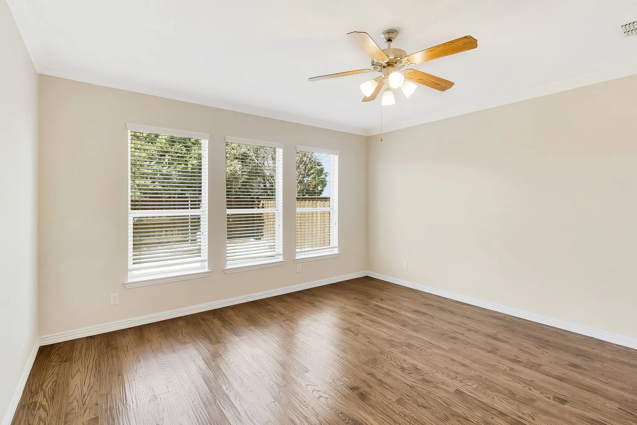 Wood-finish flooring, multiple windows with blinds, ceiling fan with integrated lighting, and crown molding