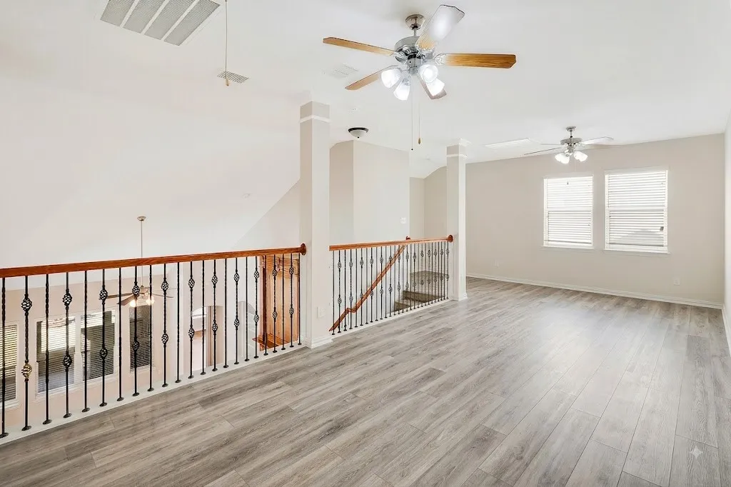 Expansive open loft area featuring wood-finish flooring, two ceiling fans with lighting, and multiple windows