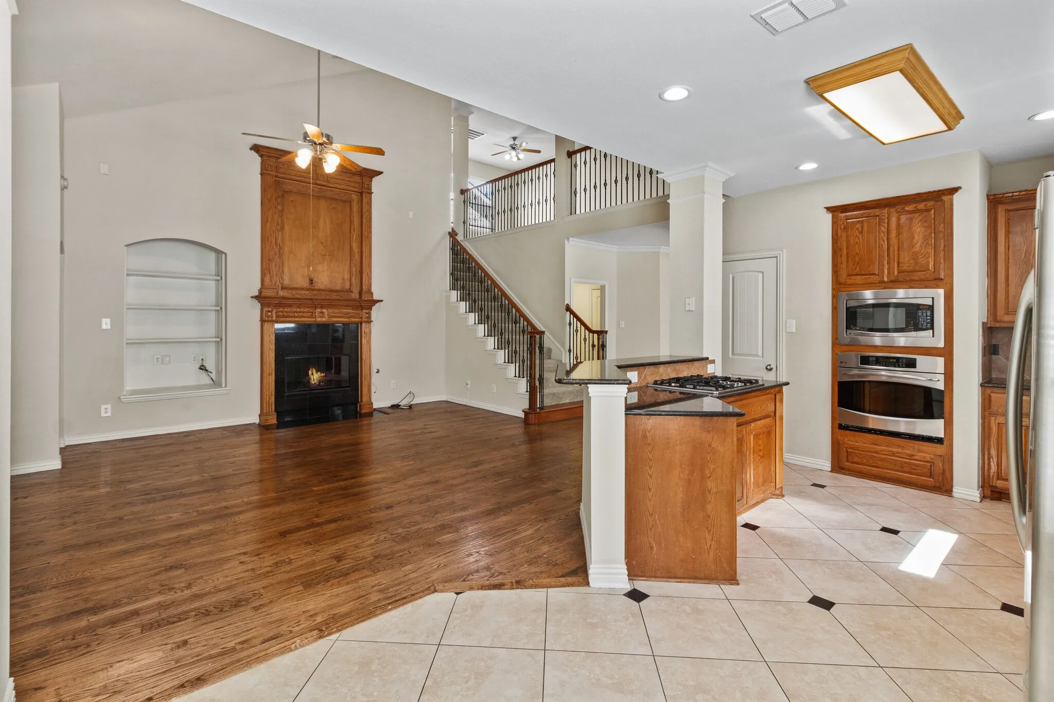 Vaulted ceiling with ceiling fan, wood-finish flooring, built-in fireplace with wood mantel, kitchen with built-in stainless steel appliances, and a tiled kitchen floor