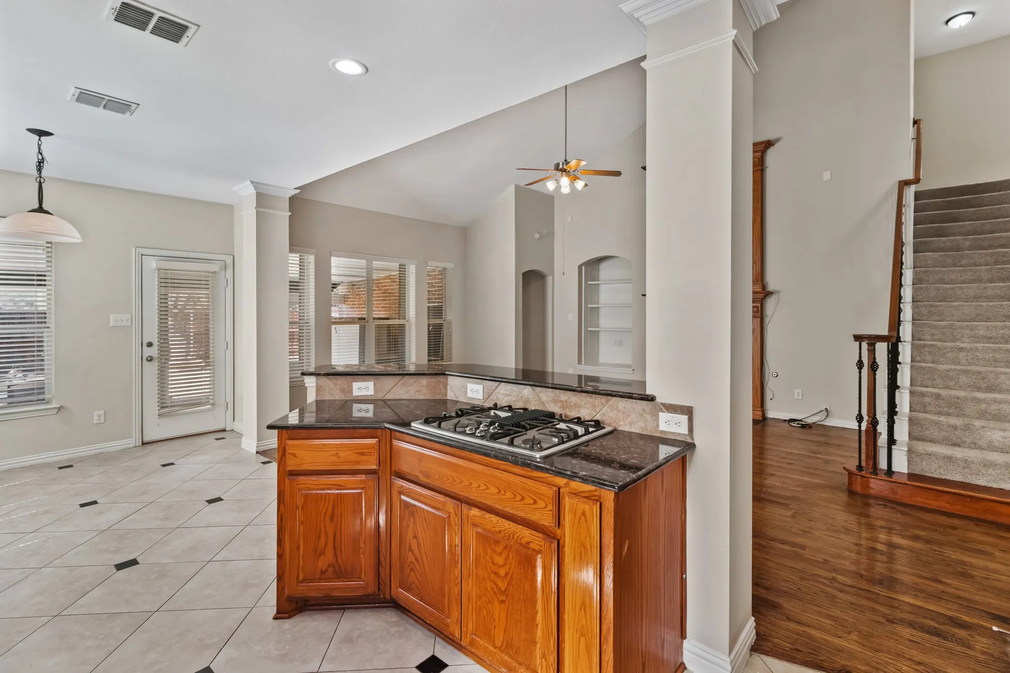 Kitchen island with built-in gas cooktop, granite countertops, tile backsplash, and wood cabinetry