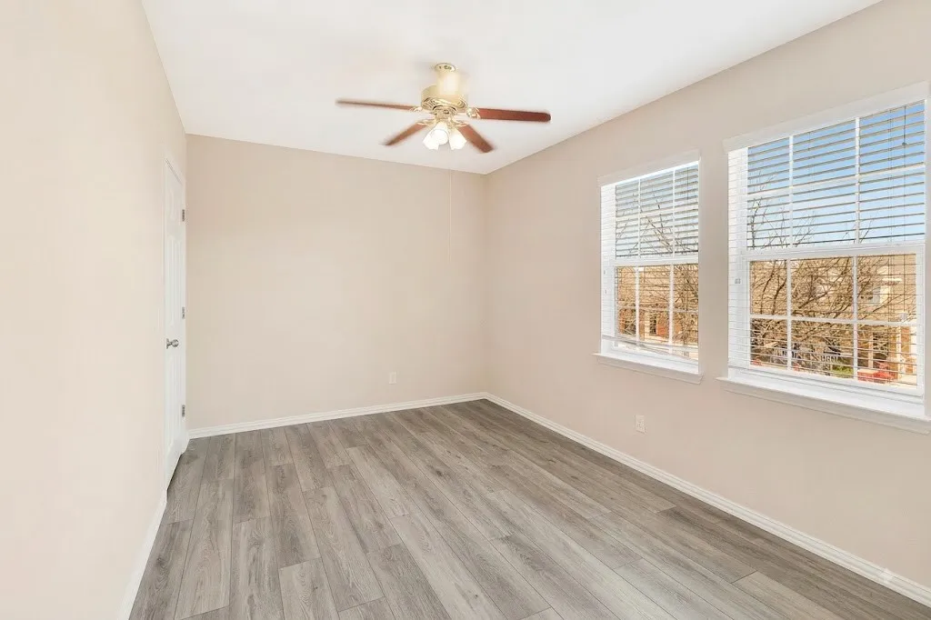 Room featuring wood-finish flooring, two windows with blinds, and a ceiling fan with integrated lighting