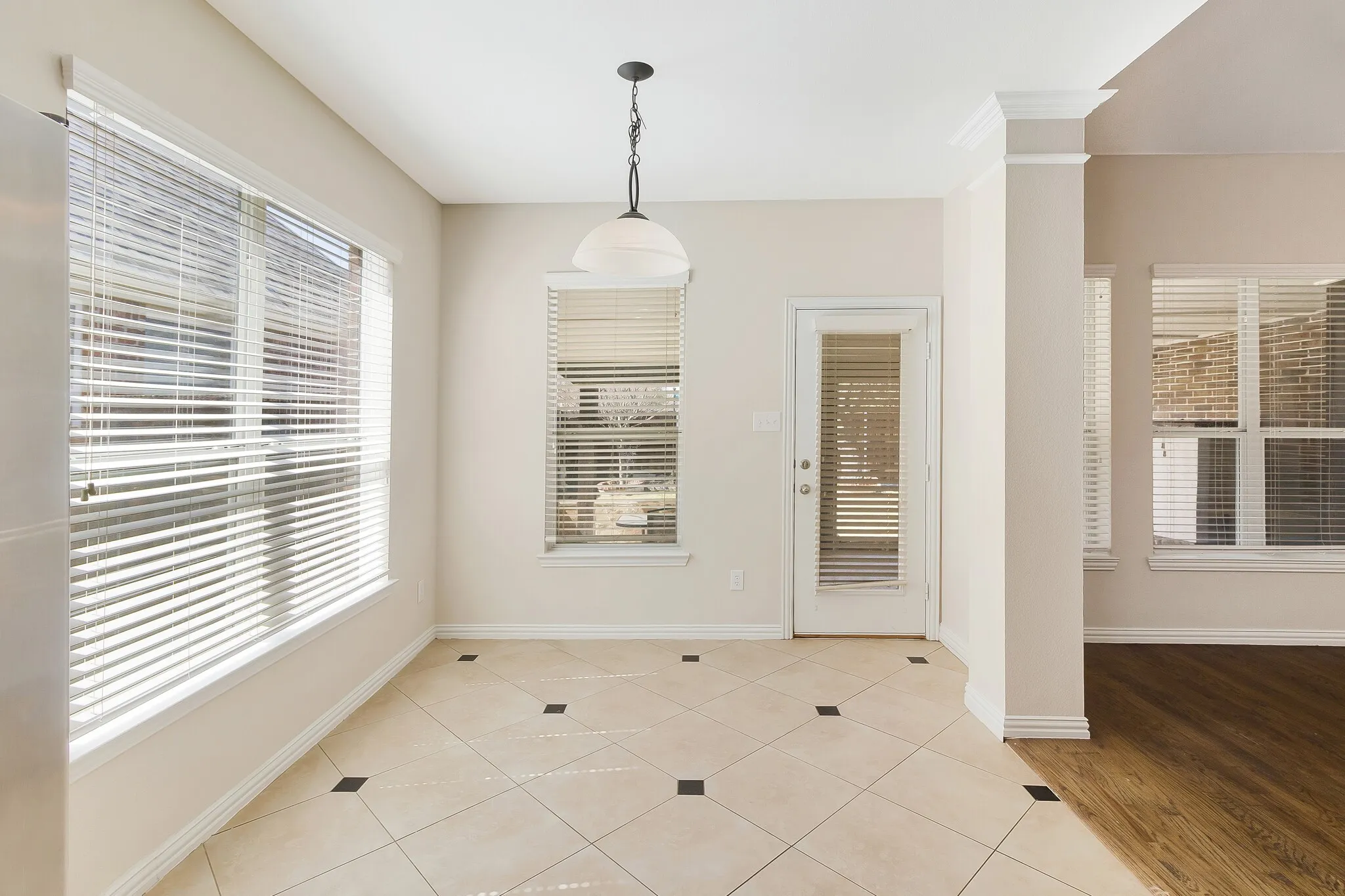 Tiled flooring with dark accent squares, multiple windows with blinds, a glass-paneled door, and a suspended ceiling fixture