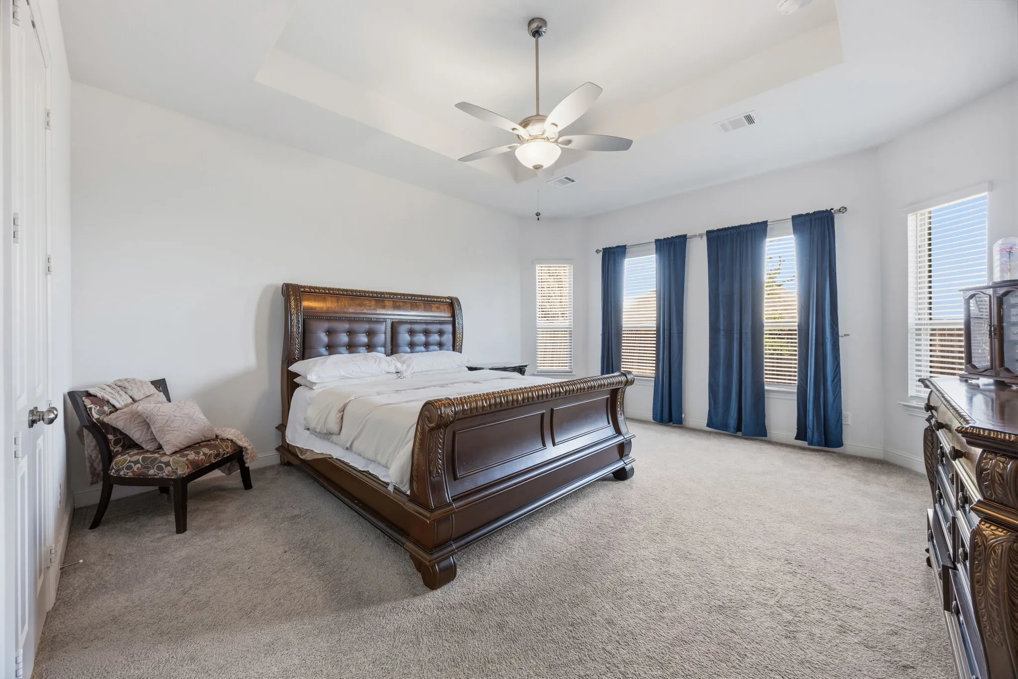 Recessed ceiling with a central fan fixture, multiple windows with blinds, and neutral carpeting