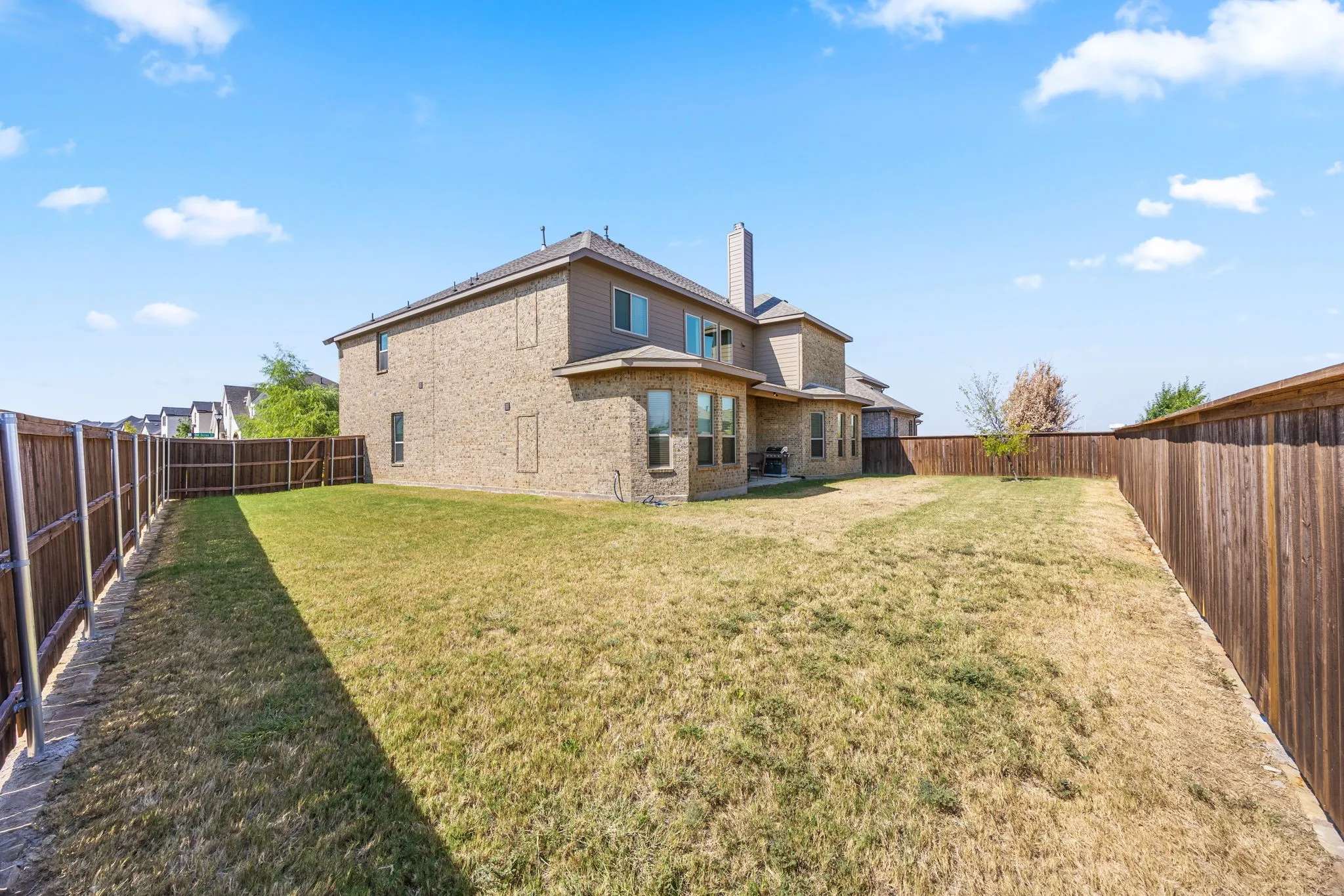 Expansive backyard with mature landscaping and level lawn space, enclosed by wood-finish fencing