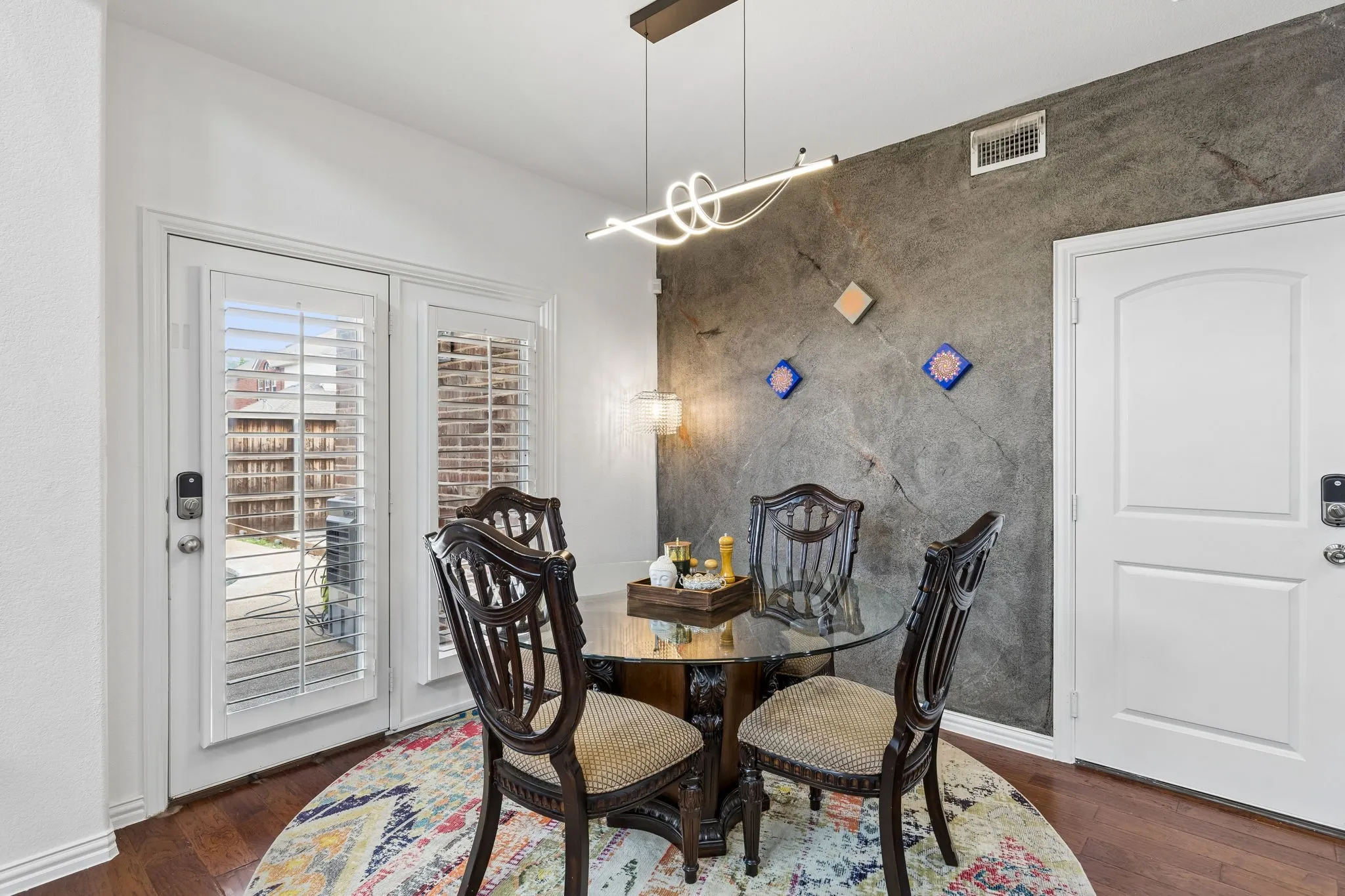 Hardwood-finish flooring, white paneled doors, textured accent wall, contemporary linear light fixture, and white plantation shutters