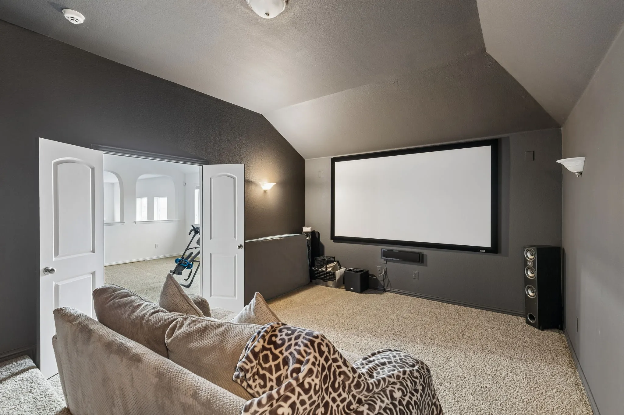 Room with sloped ceilings, wall-mounted projection screen, and recessed lighting