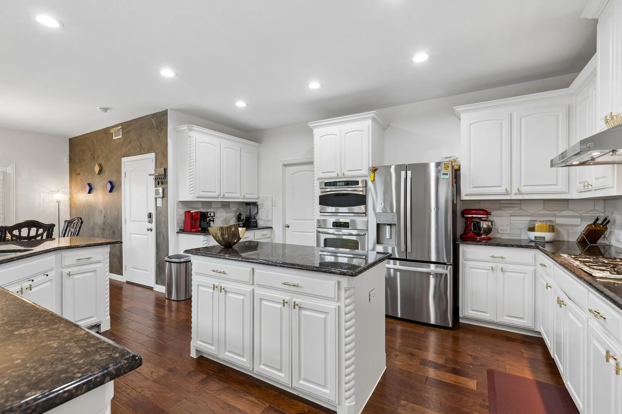 Spacious kitchen featuring white cabinetry, dark granite countertops, stainless steel appliances, a center island, and wood-finish​​‌​​​​‌​​‌‌​‌‌​​​‌‌​‌​‌​‌​​​‌​​ flooring