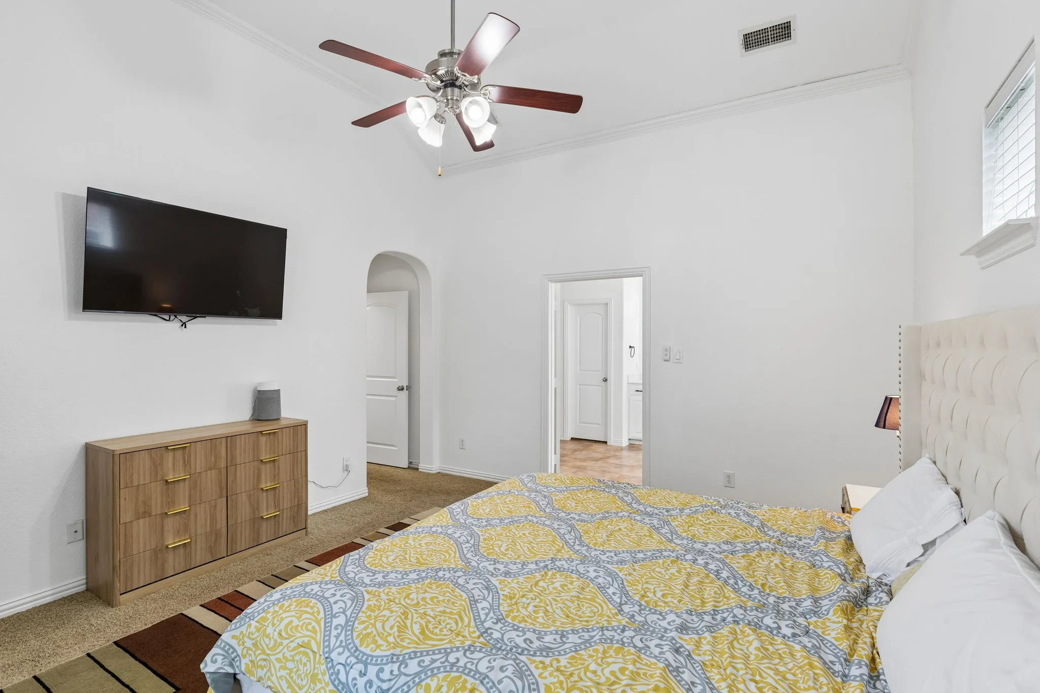 Vaulted ceiling with crown molding, ceiling fan, arched doorway, and window with blinds