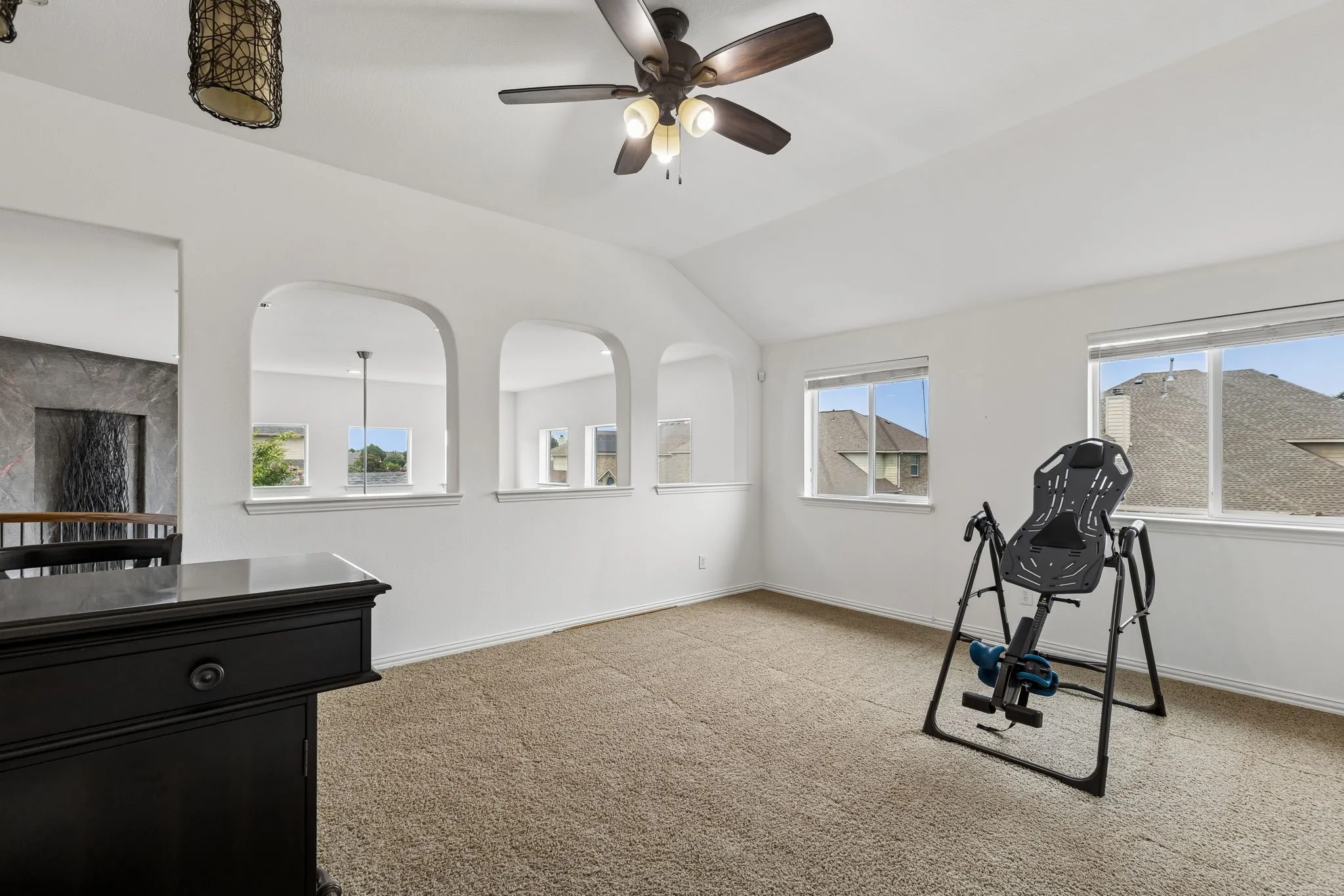 Vaulted ceiling with a ceiling fan, three arched wall openings, two windows, and neutral carpeting