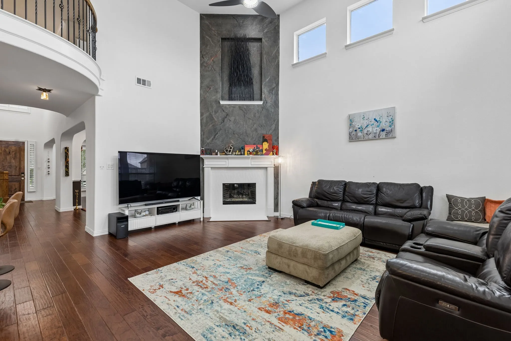 Vaulted ceilings, wood-finish flooring, a contemporary fireplace with a stone-finish facade, and a second-story balcony