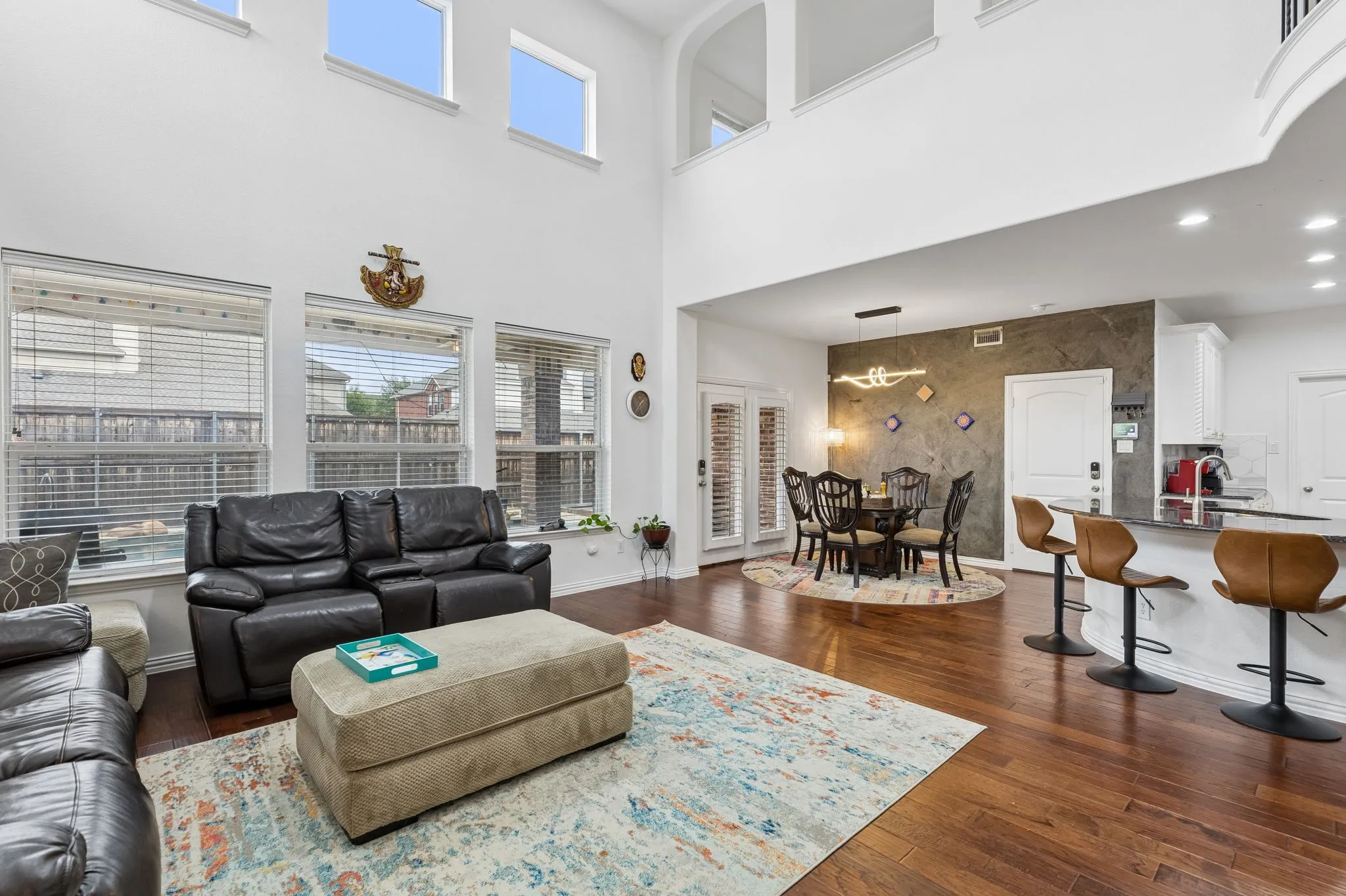 Two-story living area with high ceilings, wood-finish flooring, and multiple windows