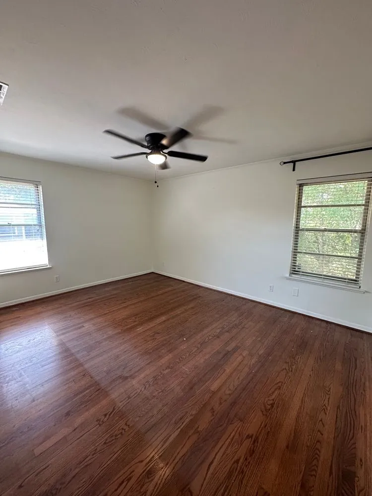 Rich hardwood flooring, neutral wall tones, ceiling fan with integrated lighting, and dual windows