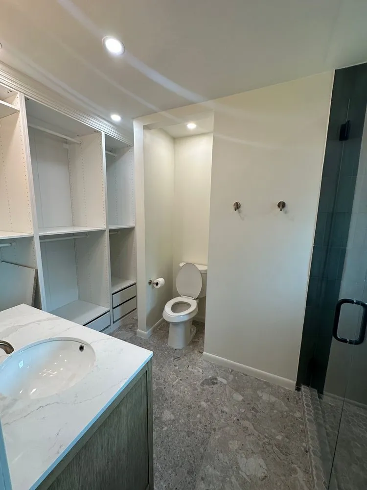 Built-in closet organization system, recessed lighting, wood-finish vanity with an integrated sink, stone-look flooring, and a glass-enclosed shower