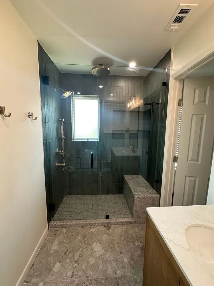 Glass-enclosed shower with multiple showerheads, a tiled bench, and a frosted window