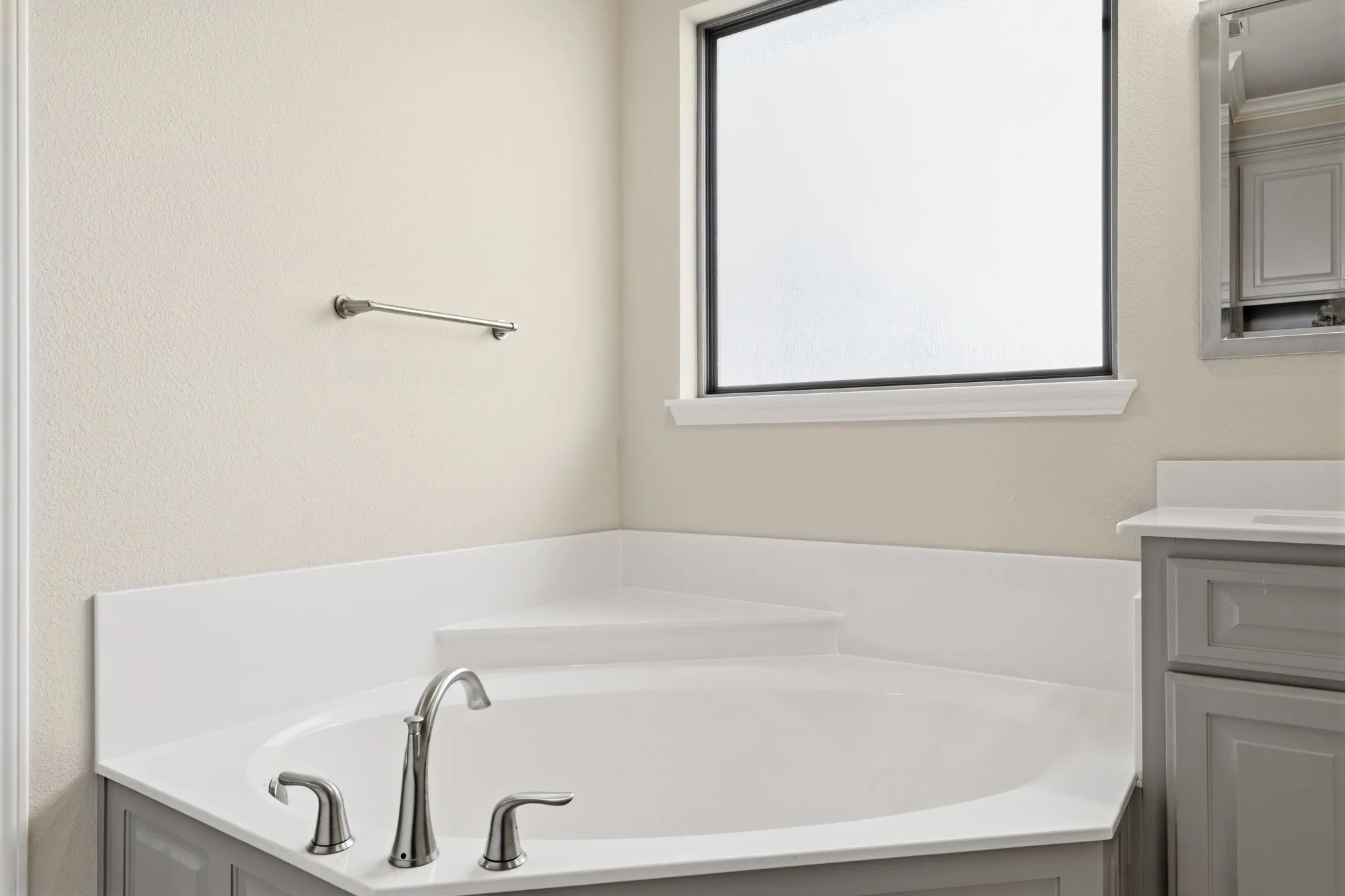 Corner soaking tub with brushed nickel fixtures, white countertop, and gray cabinetry