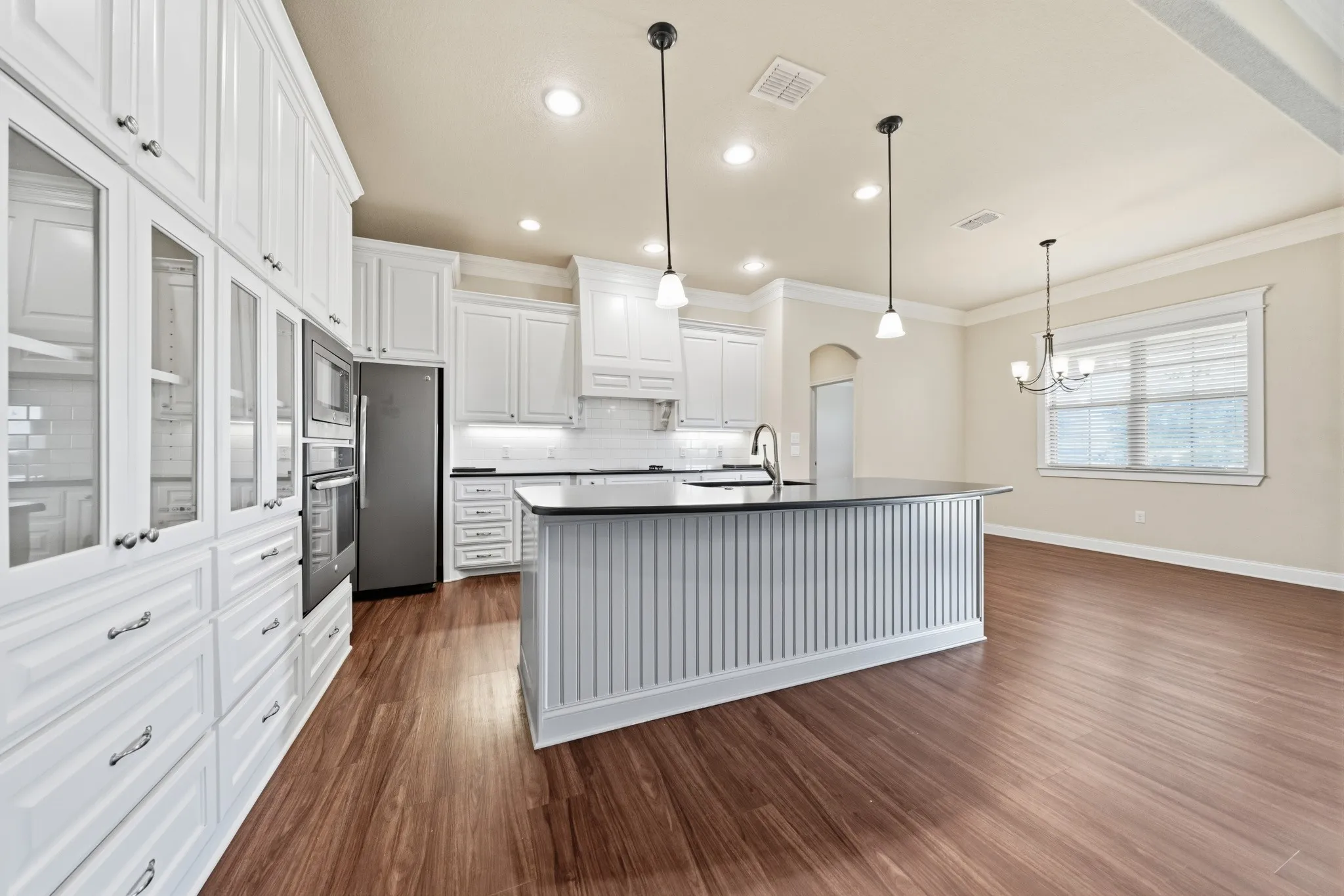 Kitchen featuring extensive white cabinetry, a center island with beadboard detailing, stone countertops, stainless steel appliances, and wood-finish flooring