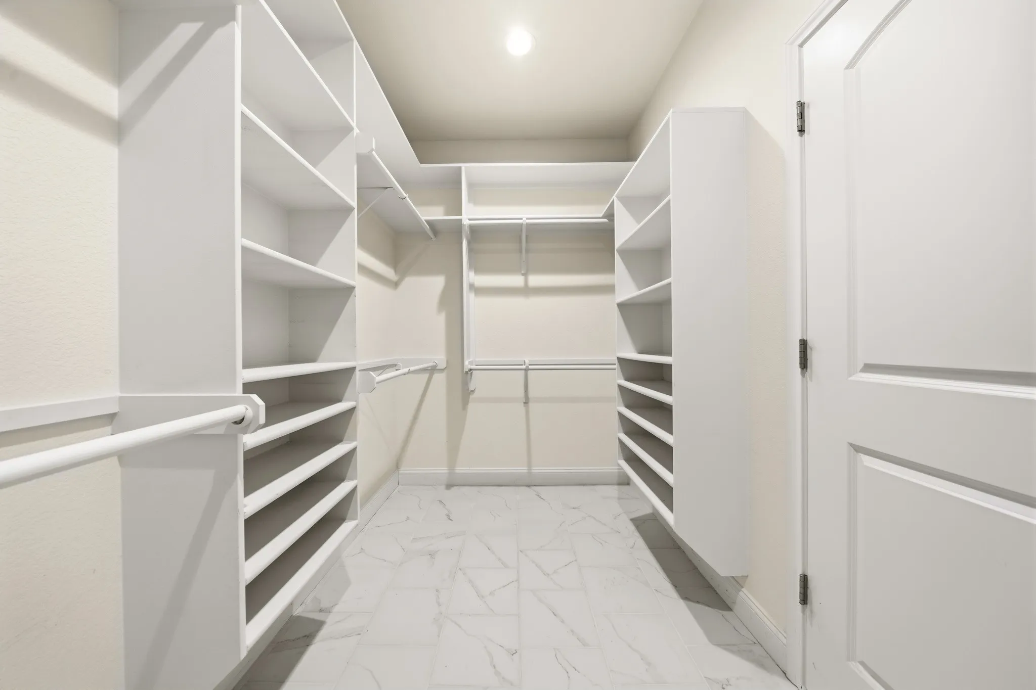 Primary suite Walk-in closet featuring built-in white shelving, integrated hanging rods, shoe racks, and white panel doors