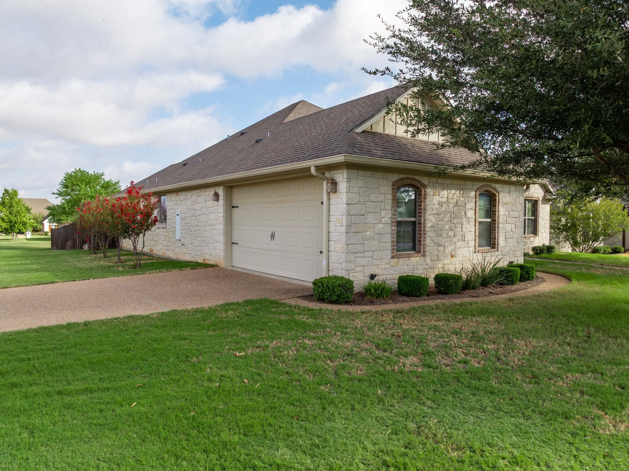 Side of Home, Austin Stone exterior with arched windows, attached garage, and well tended, mature landscaping