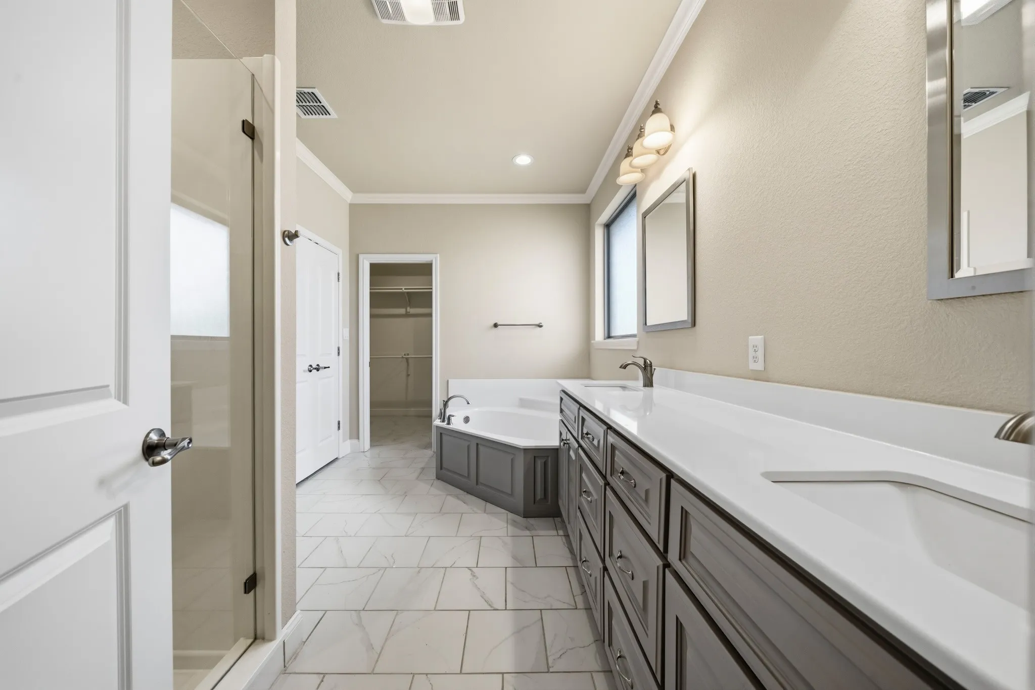 Primary bathroom with dual vanity, integrated sinks, framed mirrors, and a built-in soaking tub