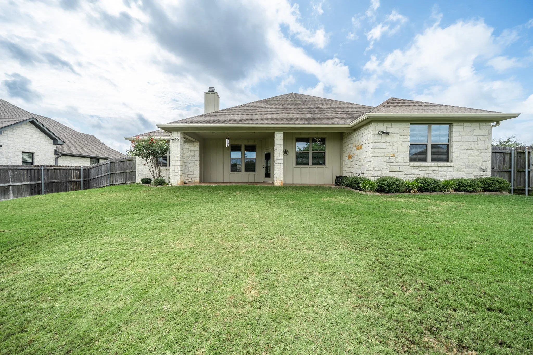 Rear of home featuring an expansive green space, stone exterior, covered patio, and a fully fenced yard