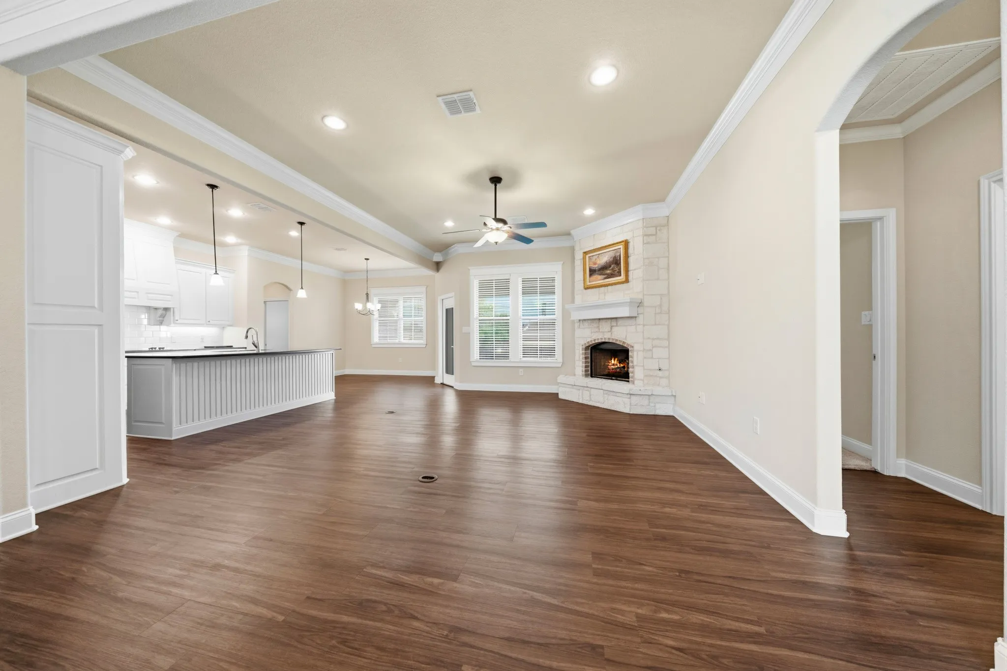 Spacious living area featuring wood-finish flooring, a corner stone-clad fireplace, and recessed lighting