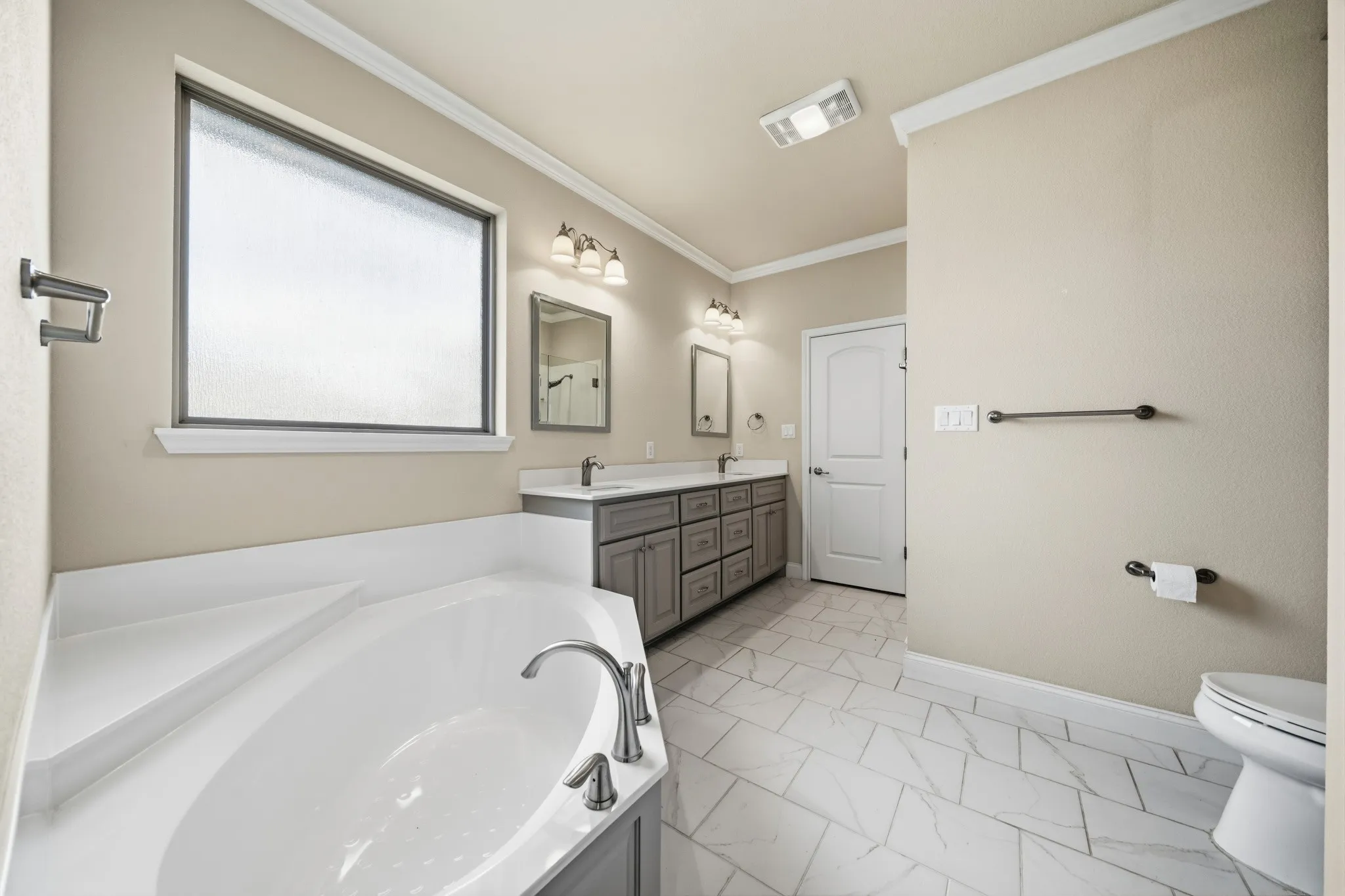 Corner soaking tub with deck-mounted fixtures, dual vanity with undermount sinks, and tiled flooring