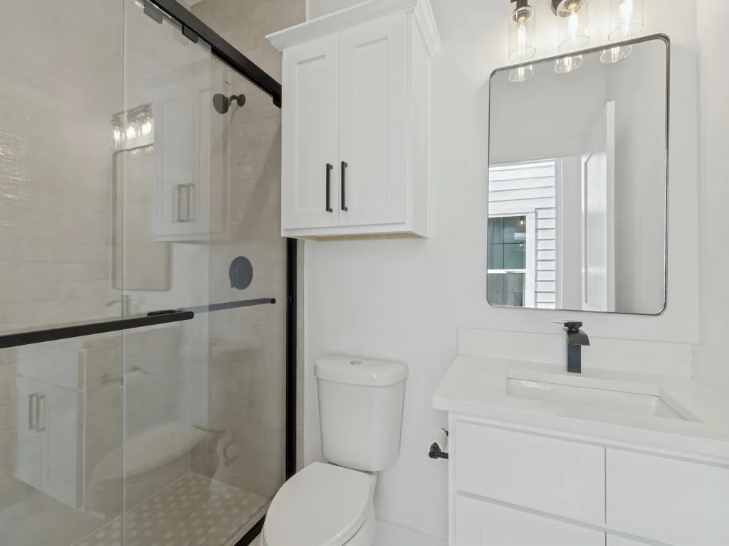 Walk-in shower with clear glass enclosure, white vanity with integrated sink, modern wall-mounted mirror, white shaker-style cabinetry, and black fixtures