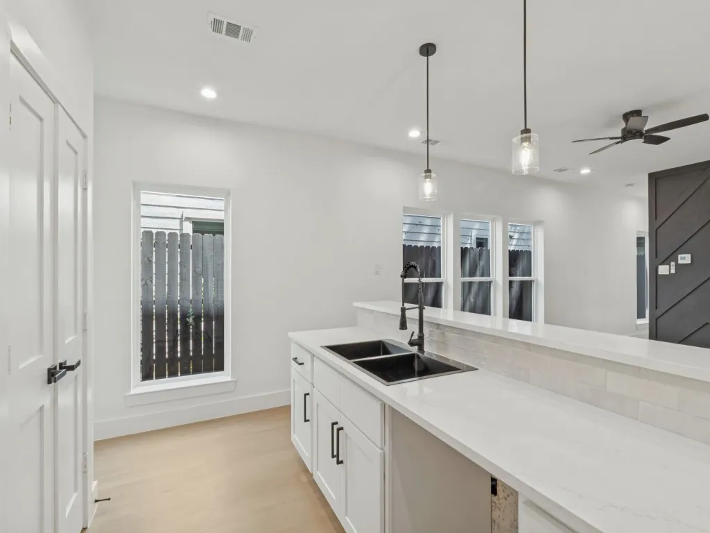 Kitchen featuring a dual basin sink with a matte black faucet, white cabinetry, integrated pendant lighting, and a ceiling fan