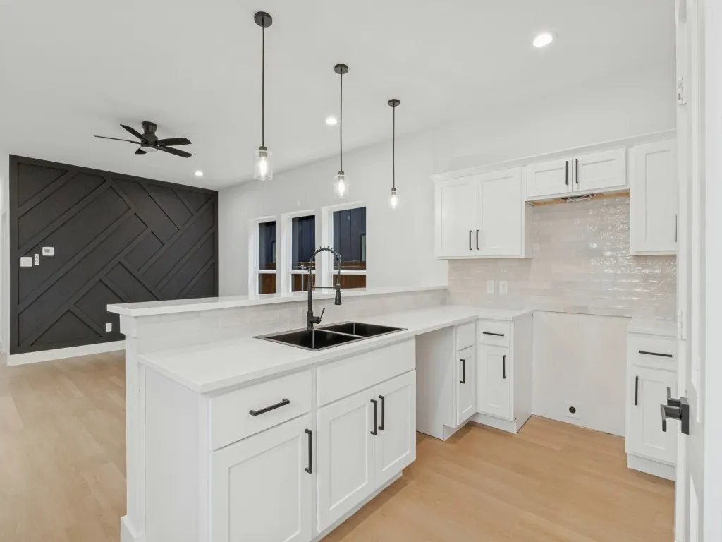 Kitchen featuring white cabinetry, quartz countertops, a double basin sink with matte black fixtures, and pendant lighting