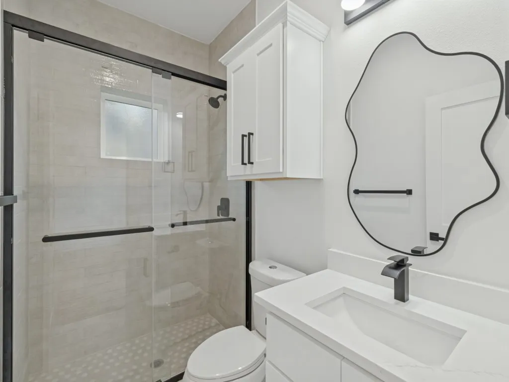 Glass-enclosed shower with matte black fixtures, integrated vanity sink with a single-handle faucet, and white cabinetry