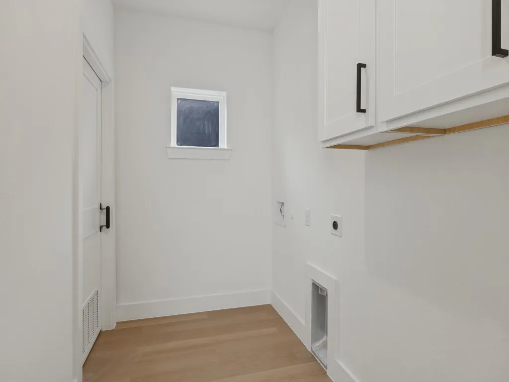 White shaker-style cabinetry with matte black hardware, wood-finish flooring, and a single window