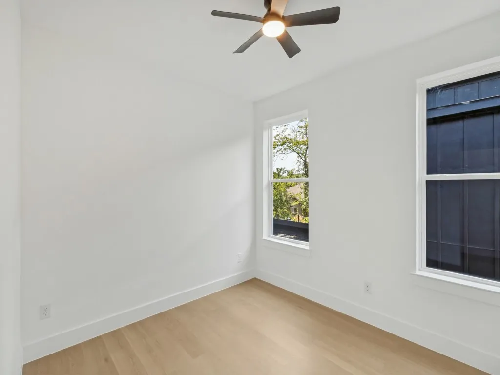 White walls, wood-finish flooring, two windows, and a ceiling fan with integrated lighting