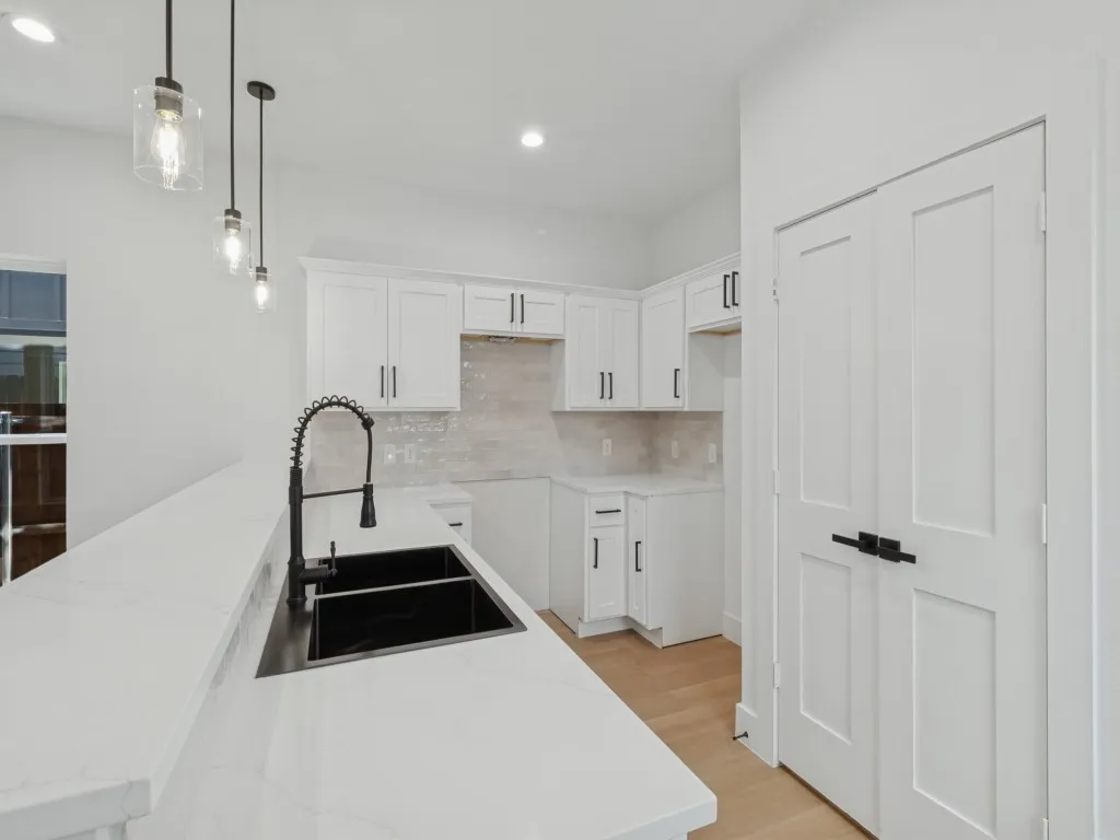 White shaker cabinetry, quartz countertops, black basin sink with gooseneck faucet, light wood-finish flooring, and pendant lighting